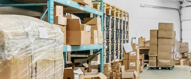 A racking aisle inside the Prep Buddies warehouse, with a shrink-wrapped pallet in the foreground and the dock door at the far end